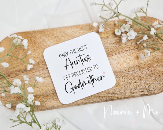 Coaster with 'Only the best Aunts get promoted to Godmother' text on a wooden board with flowers.