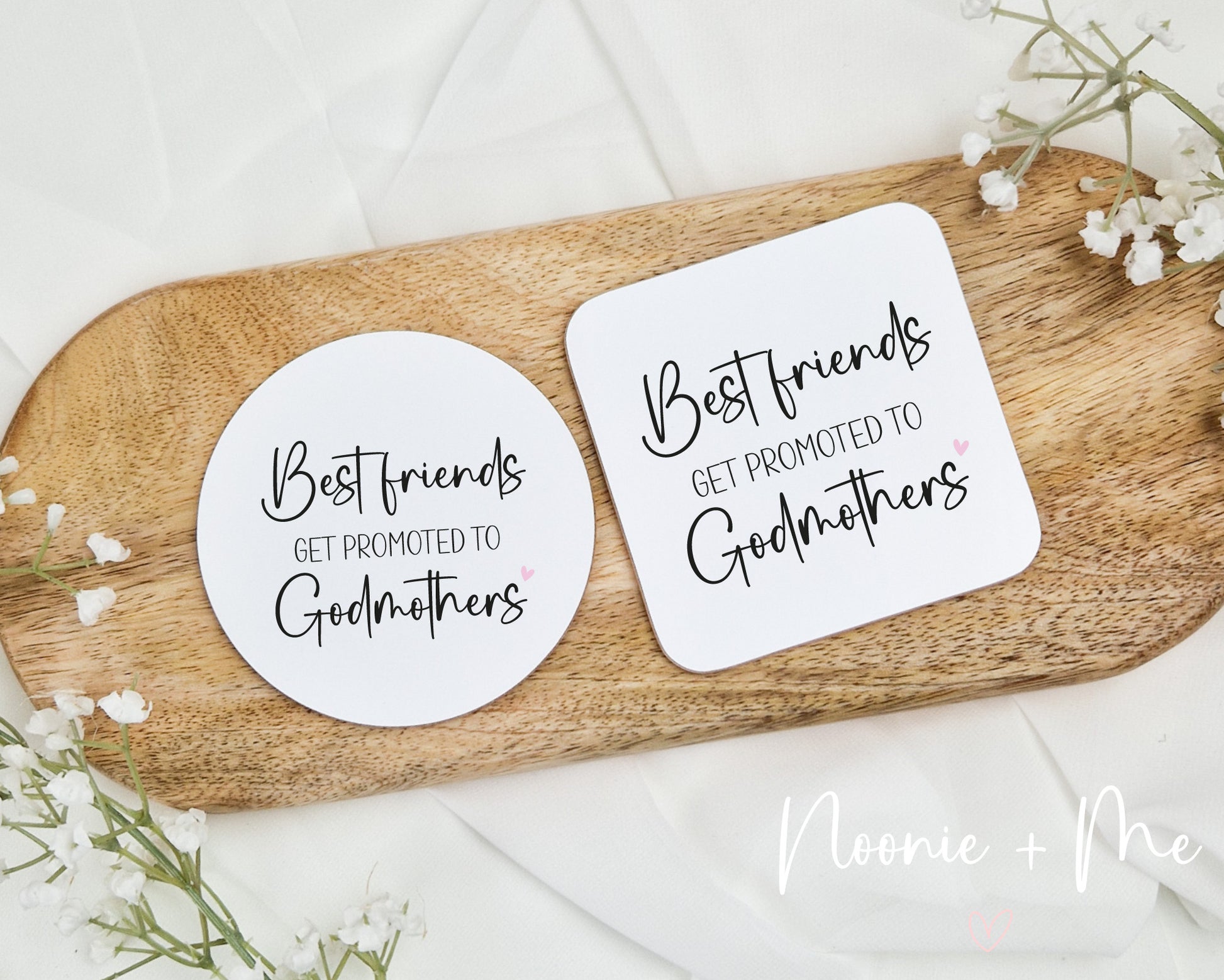 Two coasters with 'Best friends get promoted to godmothers' text on a wooden board with flowers.