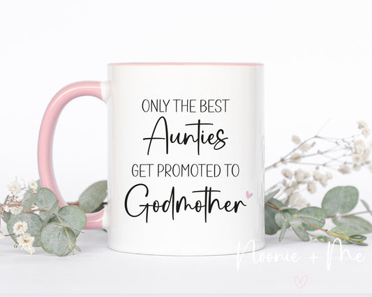 White mug with pink handle featuring text 'Only the best Aunties get promoted to Godmother' on a white background with decorative elements.